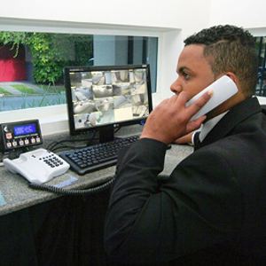 Porteiro ao telefone diante de monitores de câmeras